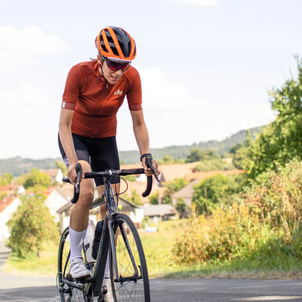 Cyclist in orange and black gear riding a bicycle on a road with greenery in the background